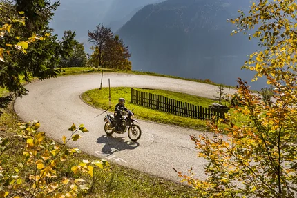 Motorradfahrer fährt durch eine kurvige Straße im herbstlichen Bergwald