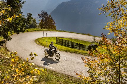 Motorradfahrer fährt durch eine kurvige Straße im herbstlichen Bergwald
