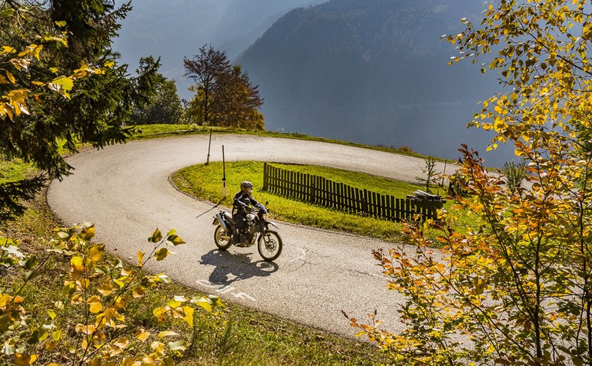 Motorrijder op een kronkelende weg in herfstachtig berglandschap