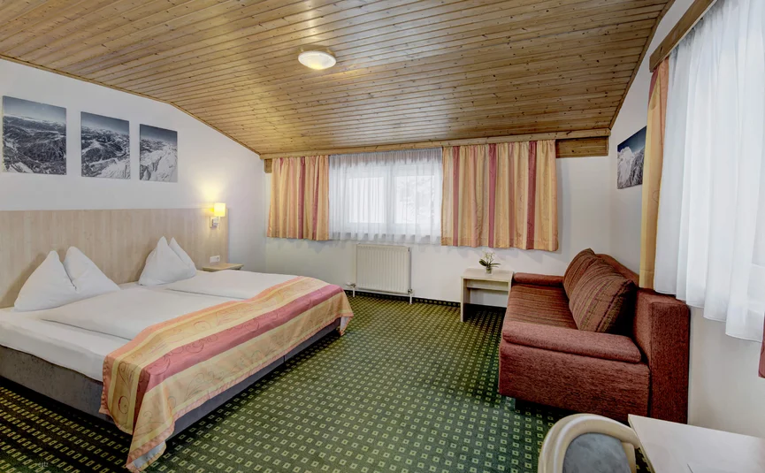 Cozy hotel room with double bed, sofa, and wooden ceiling
