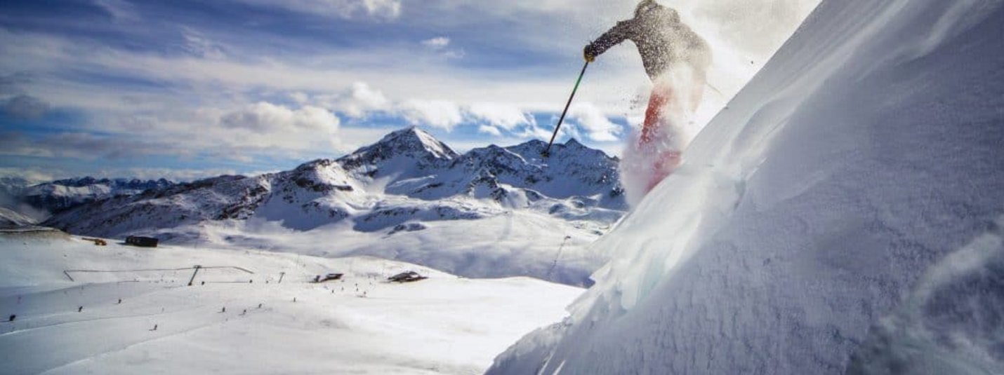 Skifahrer fährt einen steilen, schneebedeckten Hang mit Bergen im Hintergrund