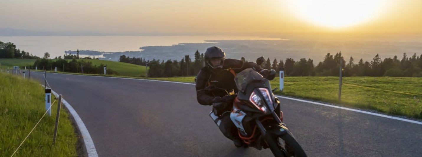 Allgäu Trip Motorradfahrer fährt bei Sonnenuntergang auf kurviger Landstraße