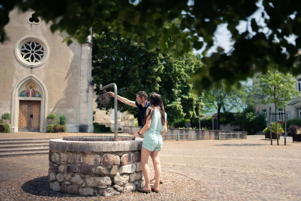 Two people at a stone fountain near a church on a sunny day