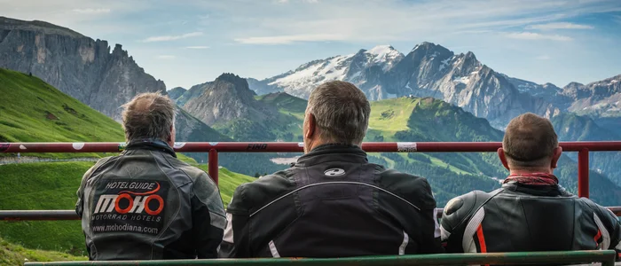Three men in motorcycle jackets sitting and viewing the Alpine mountains