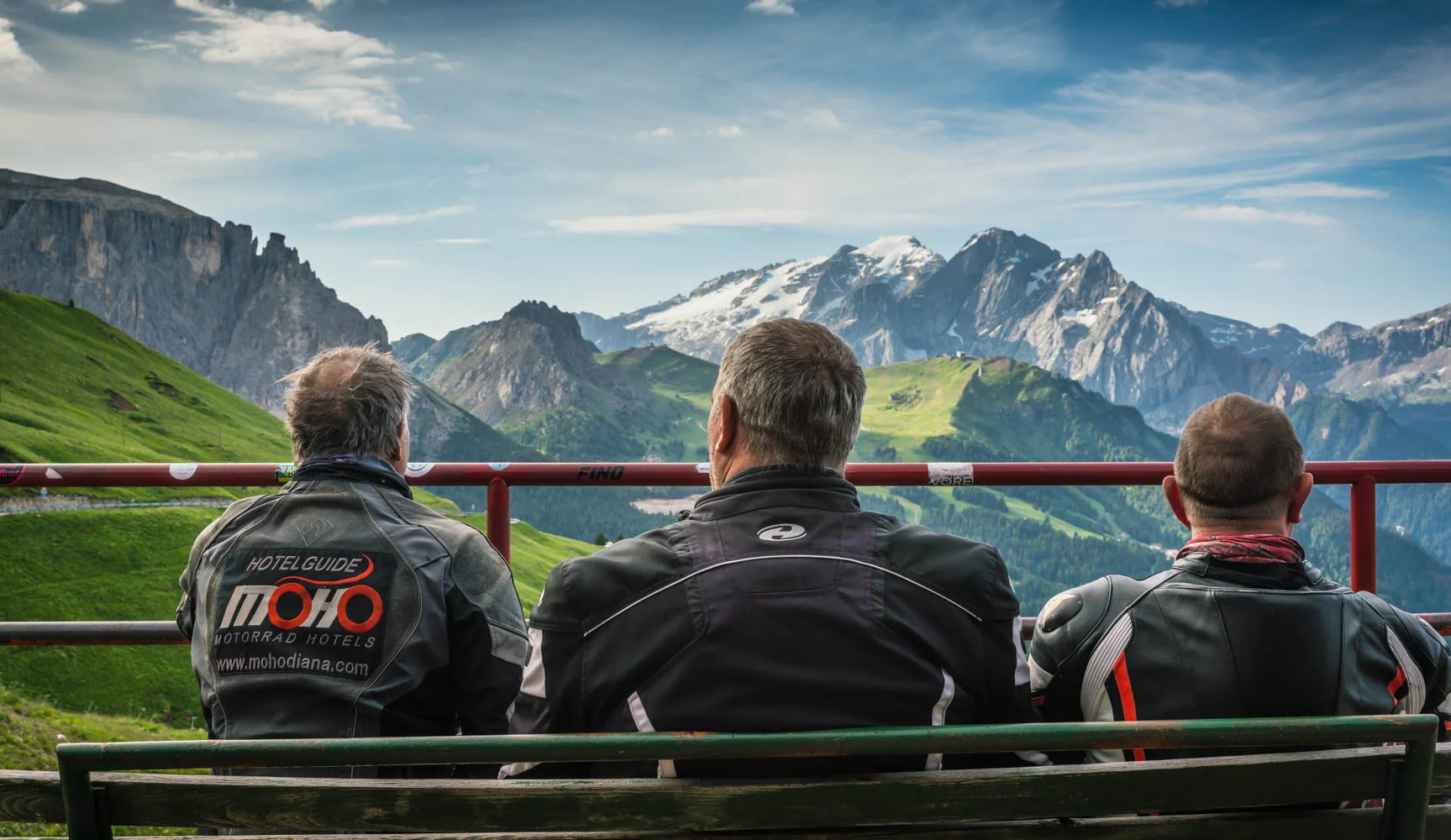 Drei Männer in Motorradjacken sitzen und schauen auf die Alpenlandschaft