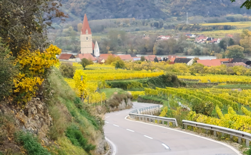 Geschwungene Landstraße mit Dorf und Bergen im Hintergrund