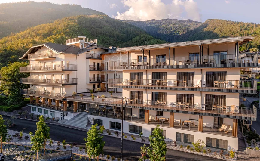 Cristallo Sport & Wellness Hotel **** © Andrea Acler Modernes Hotelgebäude mit Balkonen vor bewaldetem Berg im Sonnenlicht