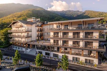 Modern hotel building with balconies set against a forested mountain in sunlight