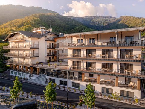 Modern hotel building with balconies set against a forested mountain in sunlight