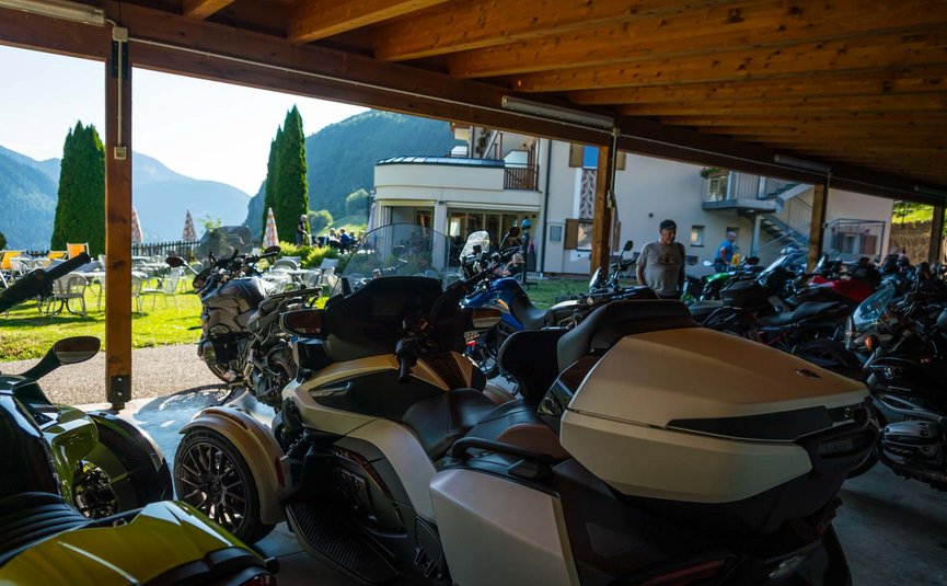 Mehrere Motorräder unter einem Holzdach vor einem Gebäude in den Bergen