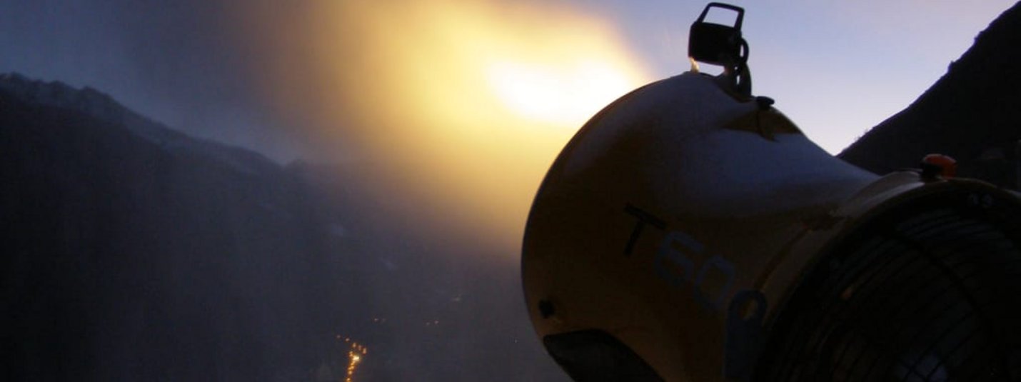 Schneekanone stößt Nebel in verschneiter Berglandschaft aus bei Abendlicht