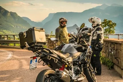 Zwei Motorradfahrer stehen nebeneinander auf einer Bergstraße mit Motorrädern