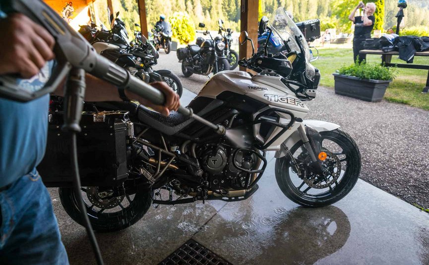 Person wäscht weiße Triumph Tiger Motorrad mit Hochdruckreiniger