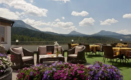 Terrasse mit Korbsesseln, Tischen und Bergblick bei sonnigem Wetter