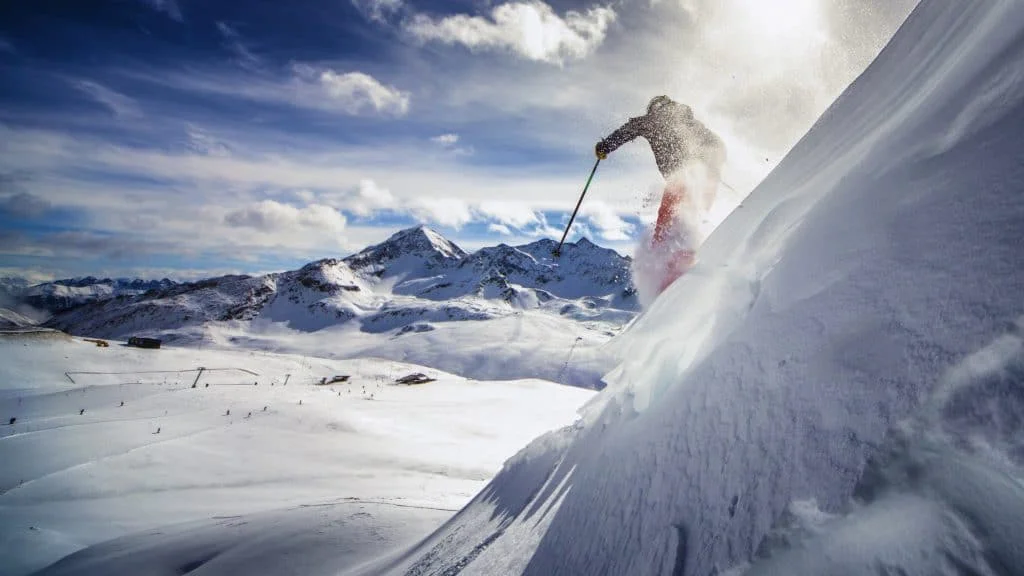 Skifahrer springt über eine verschneite Piste vor Bergpanorama