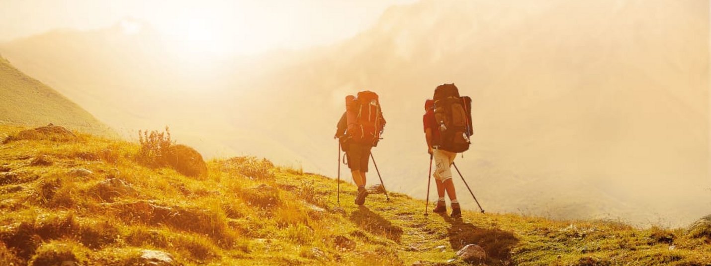 Aktivurlaub für Erlebnissammler - 7 Nächte Zwei Wanderer mit Rucksäcken wandern auf einem Bergpfad im Sonnenlicht