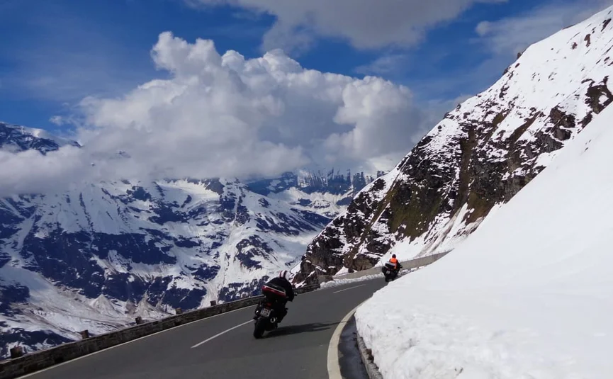 Motorrijders op een kronkelende bergweg met sneeuw en wolken