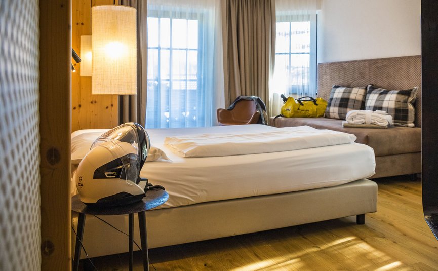 Gemütliches Hotelzimmer mit Einzelbett, Stuhl und Motorradhelm auf dem Nachttisch