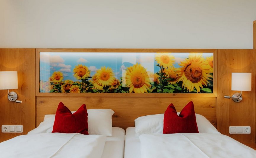 Zweibettzimmer mit Sonnenblumenbild und roten Kissen