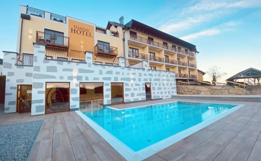 WELLNESS-TAGE am Wochenende Außenansicht des Wohlfühlhotels mit Pool und Balkonen bei klarem Himmel