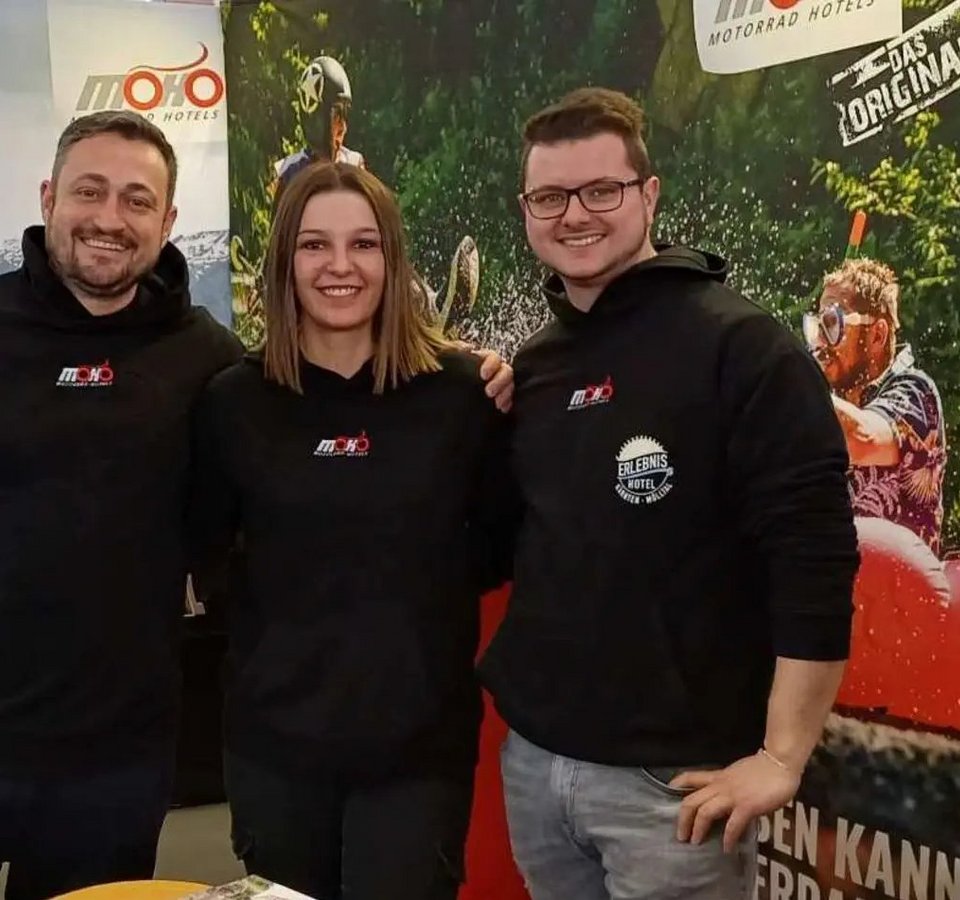 Drei Personen an einem Messestand für MoHo Motorrad Hotels