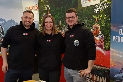 Drei Personen an einem Messestand für MoHo Motorrad Hotels
