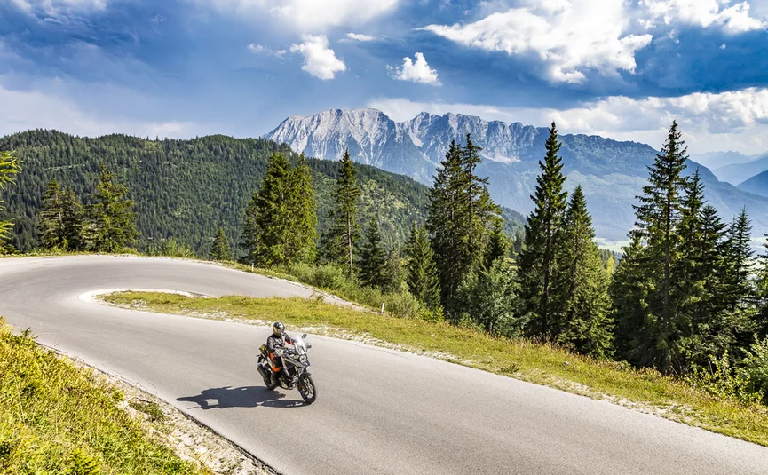 Motorcyclist on winding mountain road with pine trees and mountains behind