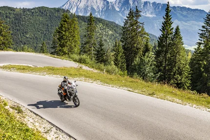 Motorradfahrer auf kurviger Bergstraße mit Tannen und Bergen im Hintergrund