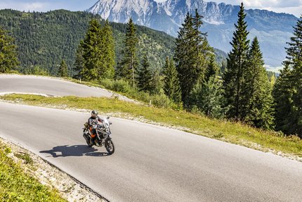 Motorradfahrer auf kurviger Bergstraße mit Tannen und Bergen im Hintergrund
