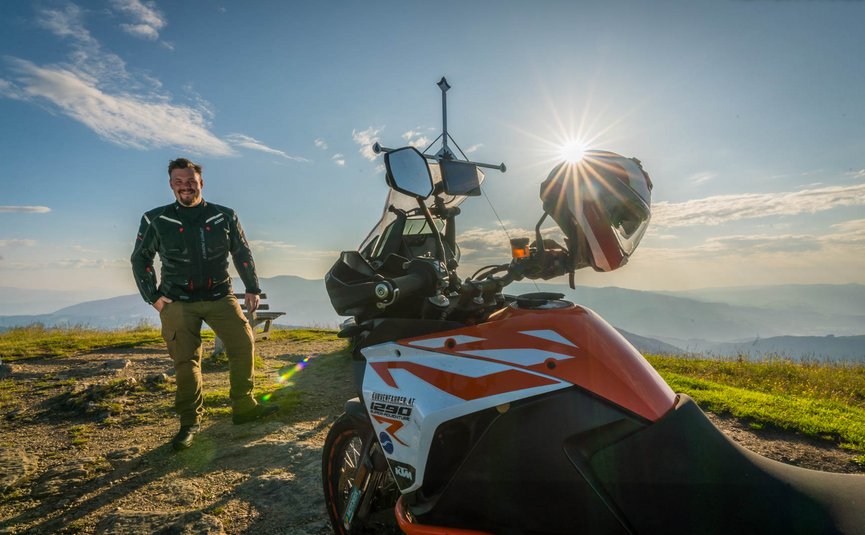 Motorradfahrer steht neben seinem KTM Motorrad auf einem Berg bei Sonnenuntergang