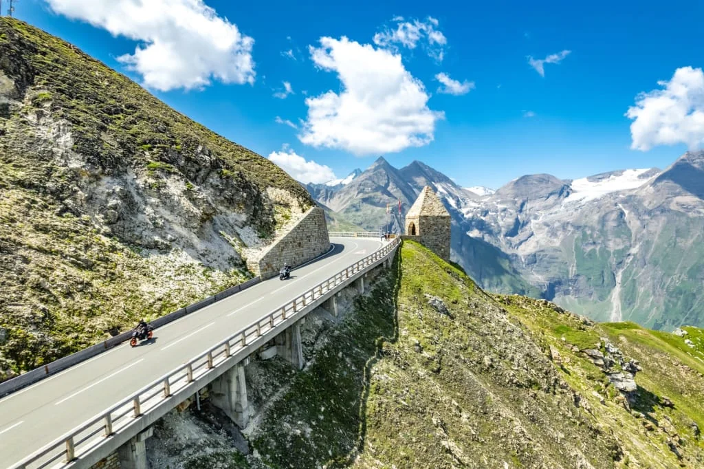 Mountain pass road with motorcyclists and snowy peaks in the distance