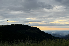 Berg mit Windrädern und bewölktem Himmel bei Sonnenuntergang