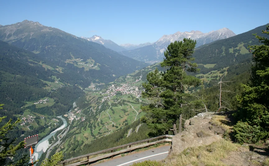 View of a valley with river, mountain villages, and forested mountains under clear sky