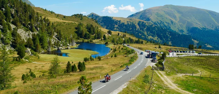 Mountain road with motorcyclists, lake, and forested hills in summer