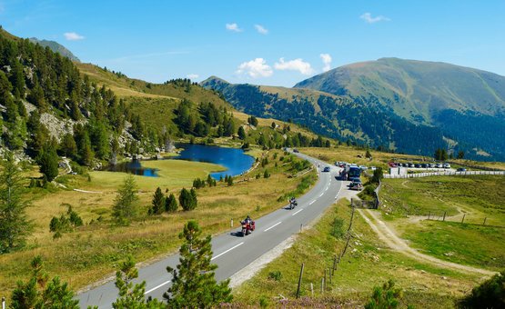 Motorradurlaub in den Niederen Tauern – Nockalm © Land Kärnten - Großglockner Hochalpenstraßen AG Gebirgsstraße mit Motorradfahrern, See und bewaldeten Bergen im Sommer