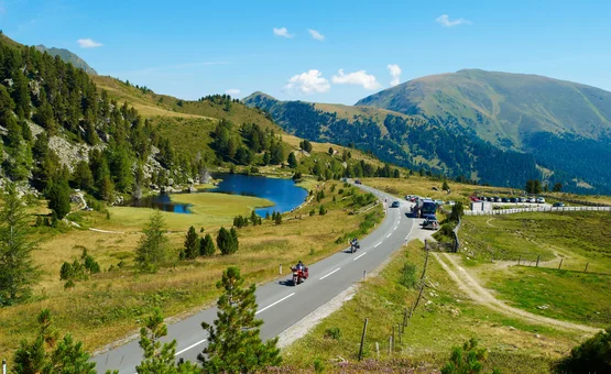 Mountain road with motorcyclists, lake, and forested hills in summer
