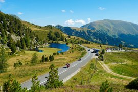 Gebirgsstraße mit Motorradfahrern, See und bewaldeten Bergen im Sommer