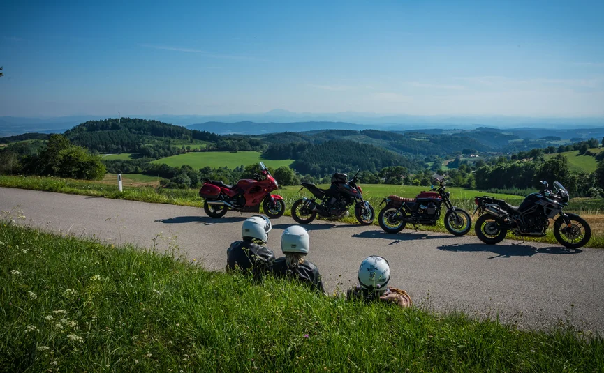 Motorvakanties in Neder-Oostenrijk © Moppetfoto.de Drie motorrijders zitten aan de weg met uitzicht op groene heuvels en blauwe bergen