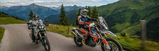 Zwei Motorradfahrer fahren auf einer Bergstraße mit Alpenpanorama