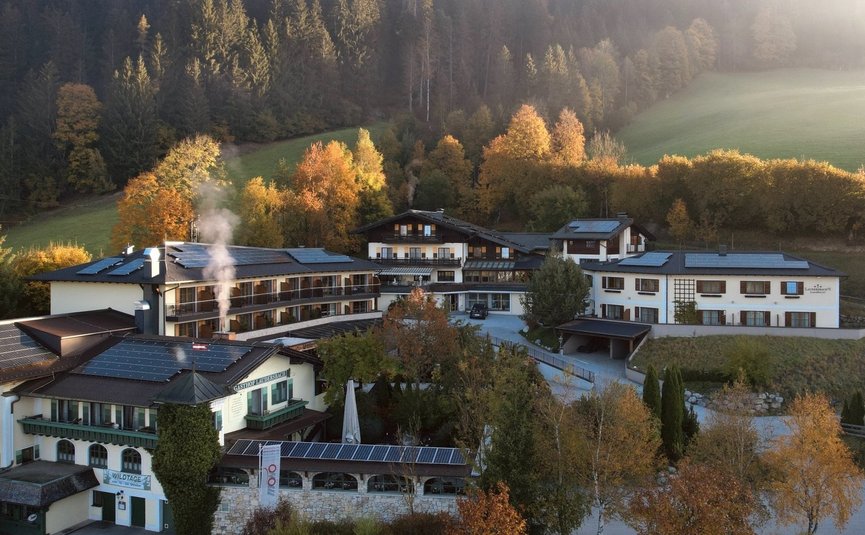 Berghotel mit Solarpaneelen umgeben von Herbstwald und Nebel