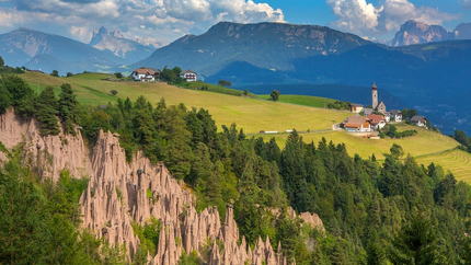 Landschaft mit Erdpyramiden, Wäldern, grünen Wiesen und Bergdorf im Hintergrund
