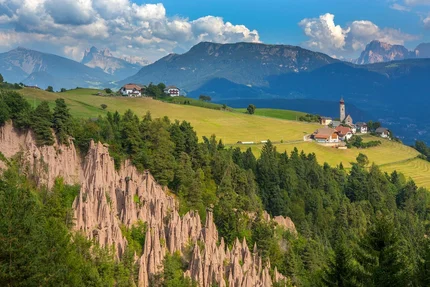Landscape with earth pyramids, forests, green meadows, and mountain village in background