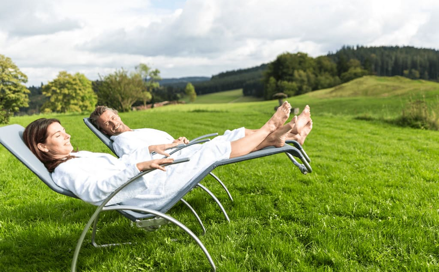 Paar entspannt in weißen Bademänteln auf Liegestühlen auf grüner Wiese