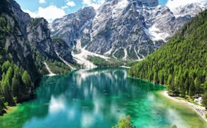 Klarer Bergsee umgeben von Tannen und schneebedeckten Gipfeln