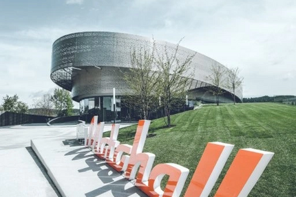 Sonnleiten 14: Chiemsee–Motohall–Deutsche Alpenstraße Modernes rundes Gebäude mit großem orange-weißen Schriftzug im Vordergrund