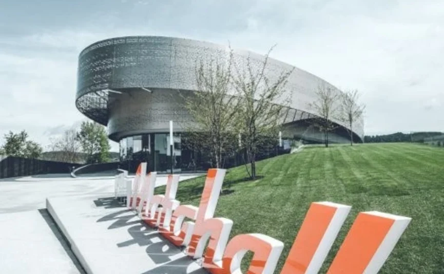 14 Hotel Sonnleiten: Chiemsee-Motohall-Duitse Alpenroute Modern rond gebouw met groot oranje-wit bord op de voorgrond