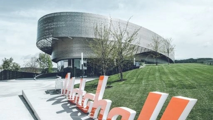 Modernes rundes Gebäude mit großem orange-weißen Schriftzug im Vordergrund