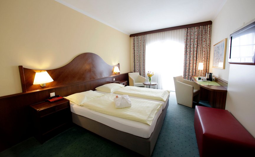 Doppelzimmer in Hotel mit zwei Betten, Schreibtisch und Fenster mit Vorhängen