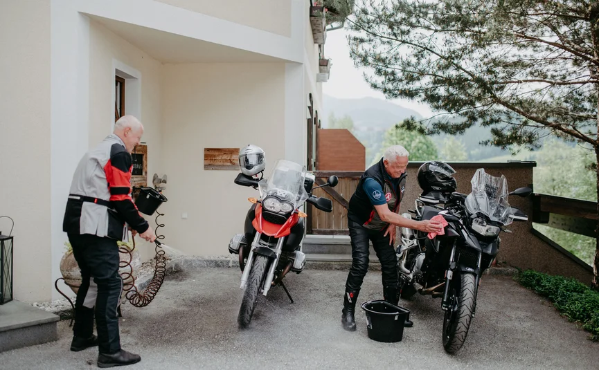 Two elderly men cleaning their motorcycles outside a house