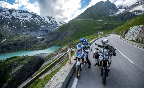 Motorvakantie in SalzburgerLand © Arturo Rivas Twee motorrijders op alpenweg met bergmeer en besneeuwde pieken